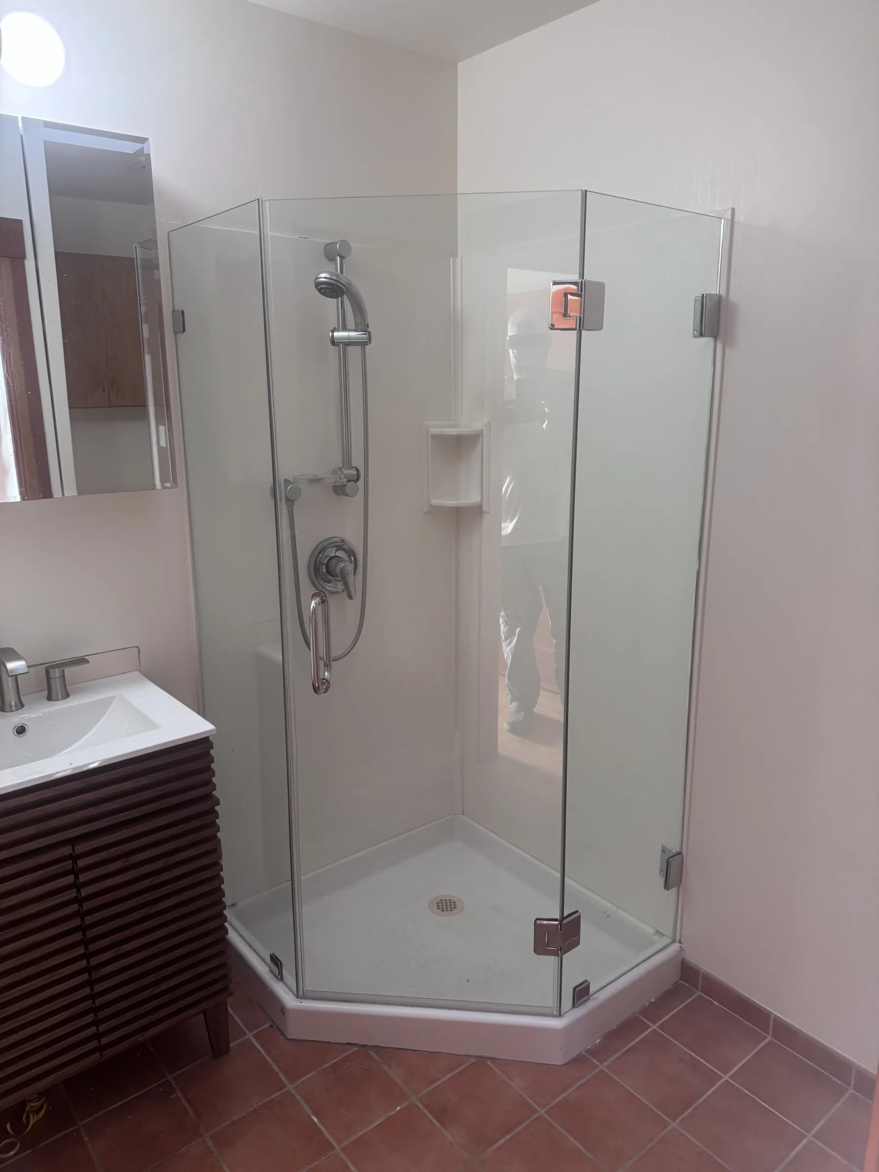 Bathroom remodel in Montclair with neo-angle corner glass shower, built-in niche, chrome fixtures, slatted wood vanity, and terracotta tile floor