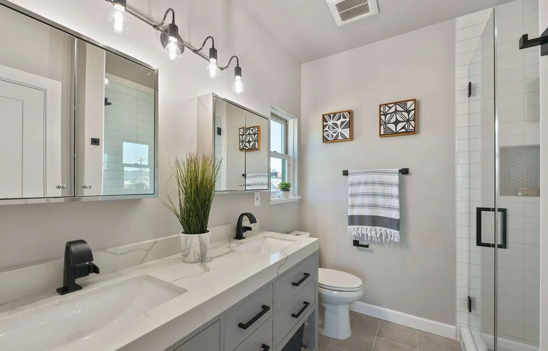 Modern bathroom with double-sink quartz vanity, matte black hardware, edison vanity lights, and glass subway-tile shower