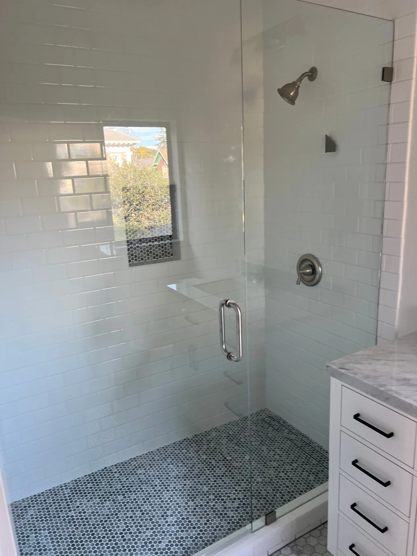 Finished walk-in shower with white subway tile walls, green pebble mosaic accent strip, and glass panel