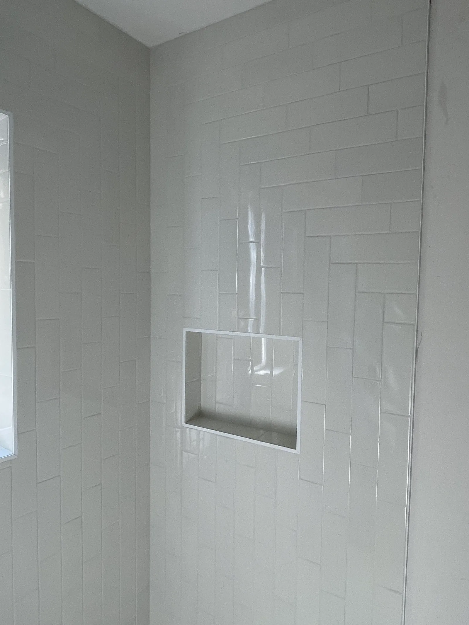 Subway tile shower niche from angle showing herringbone accent pattern