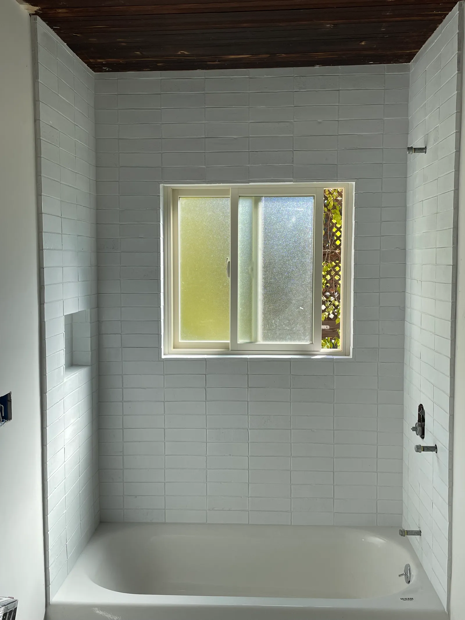 Wide view of tiled bathroom with tub, subway tile walls, and window