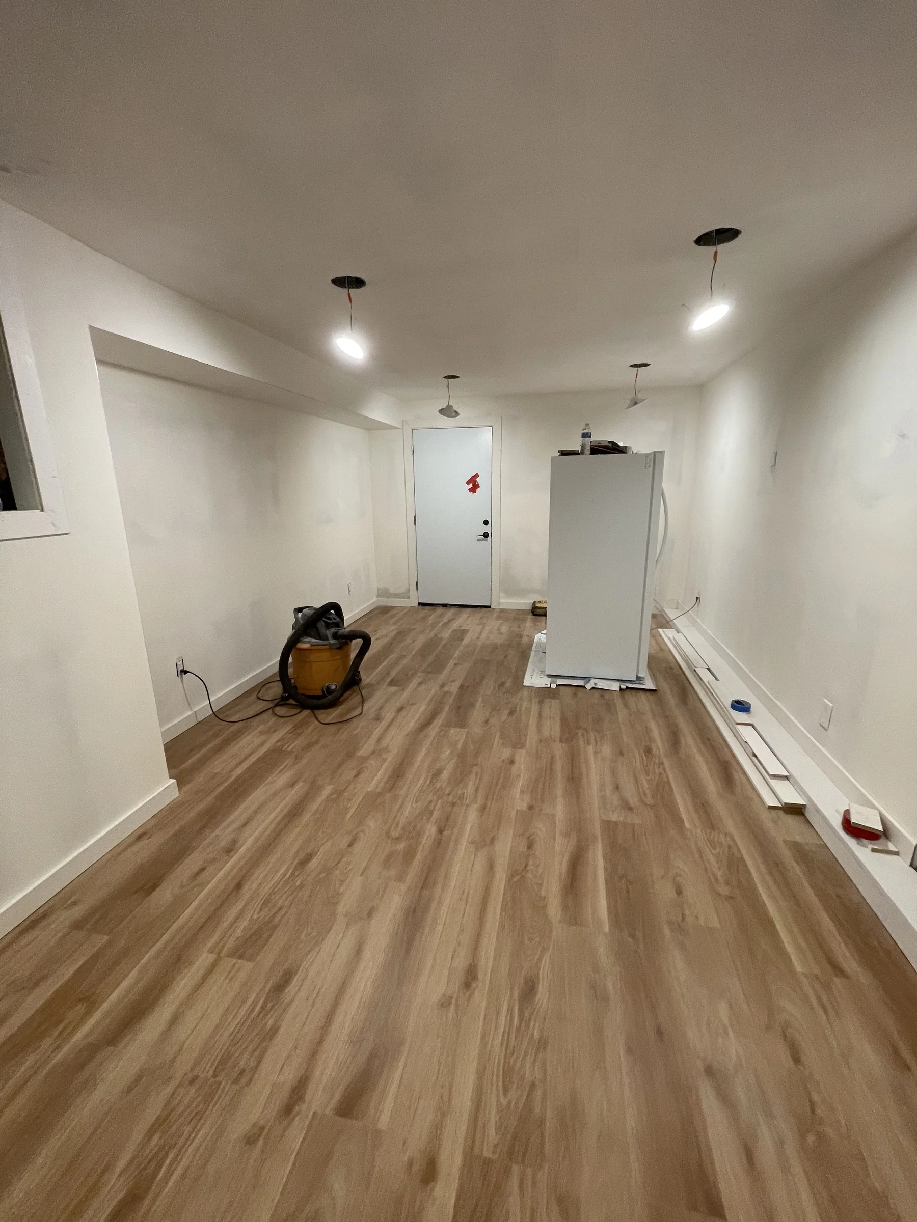 Piedmont flooring install — warm honey-toned Impala GAIA LVT wide-plank in a long lower-level room, baseboards staged for trim-out