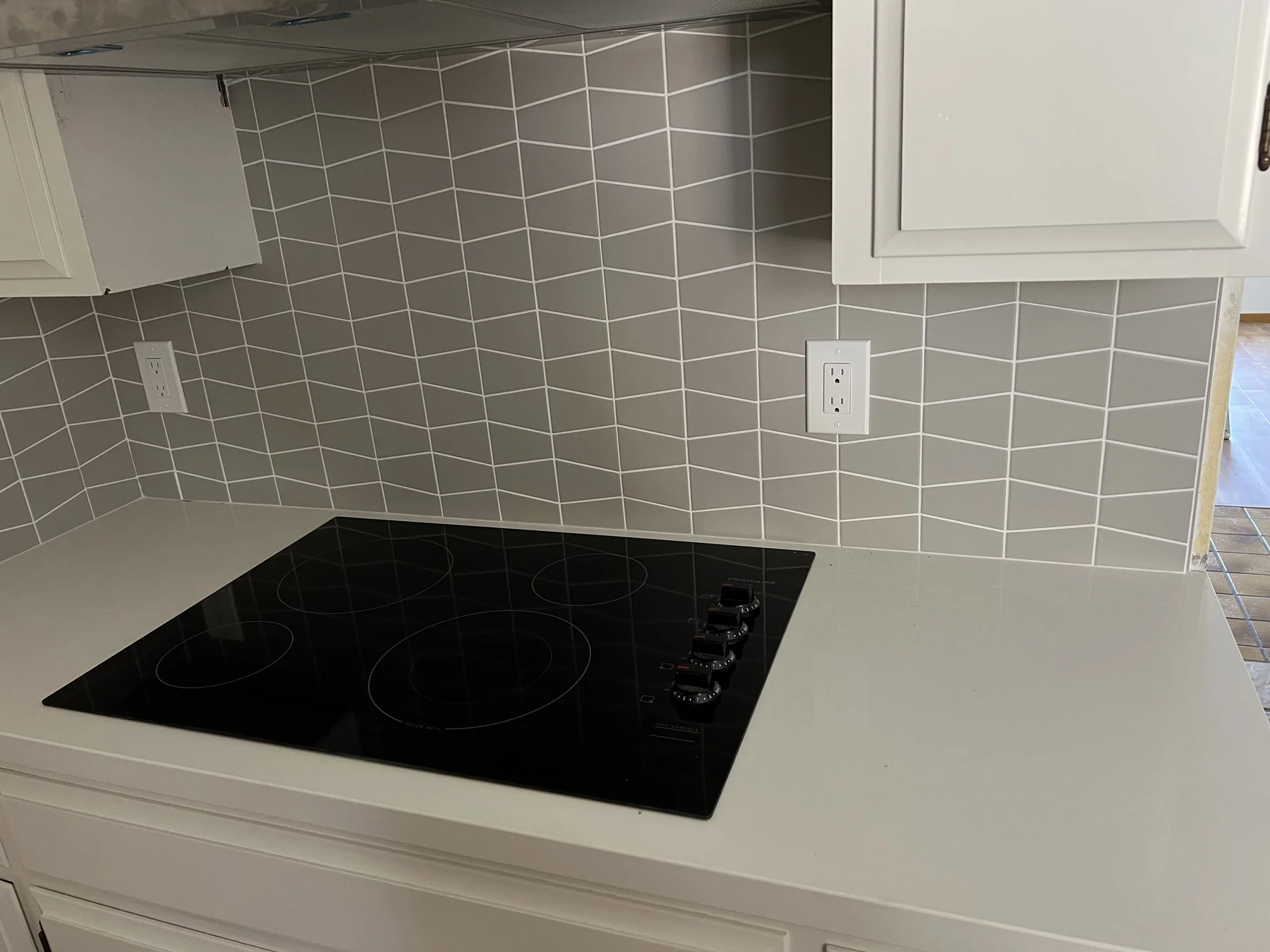 Close-up of a finished Alameda kitchen with white quartz countertop, gray chevron-pattern tile backsplash, black Frigidaire electric cooktop, and stainless range hood