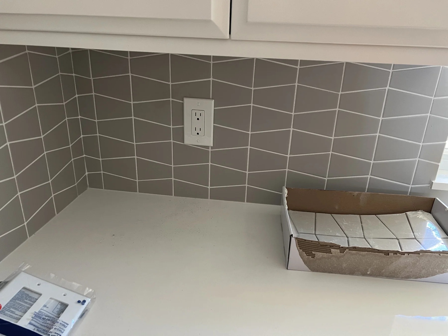Mid-install Alameda kitchen counter with white quartz and gray chevron tile backsplash, spare tile box on the counter