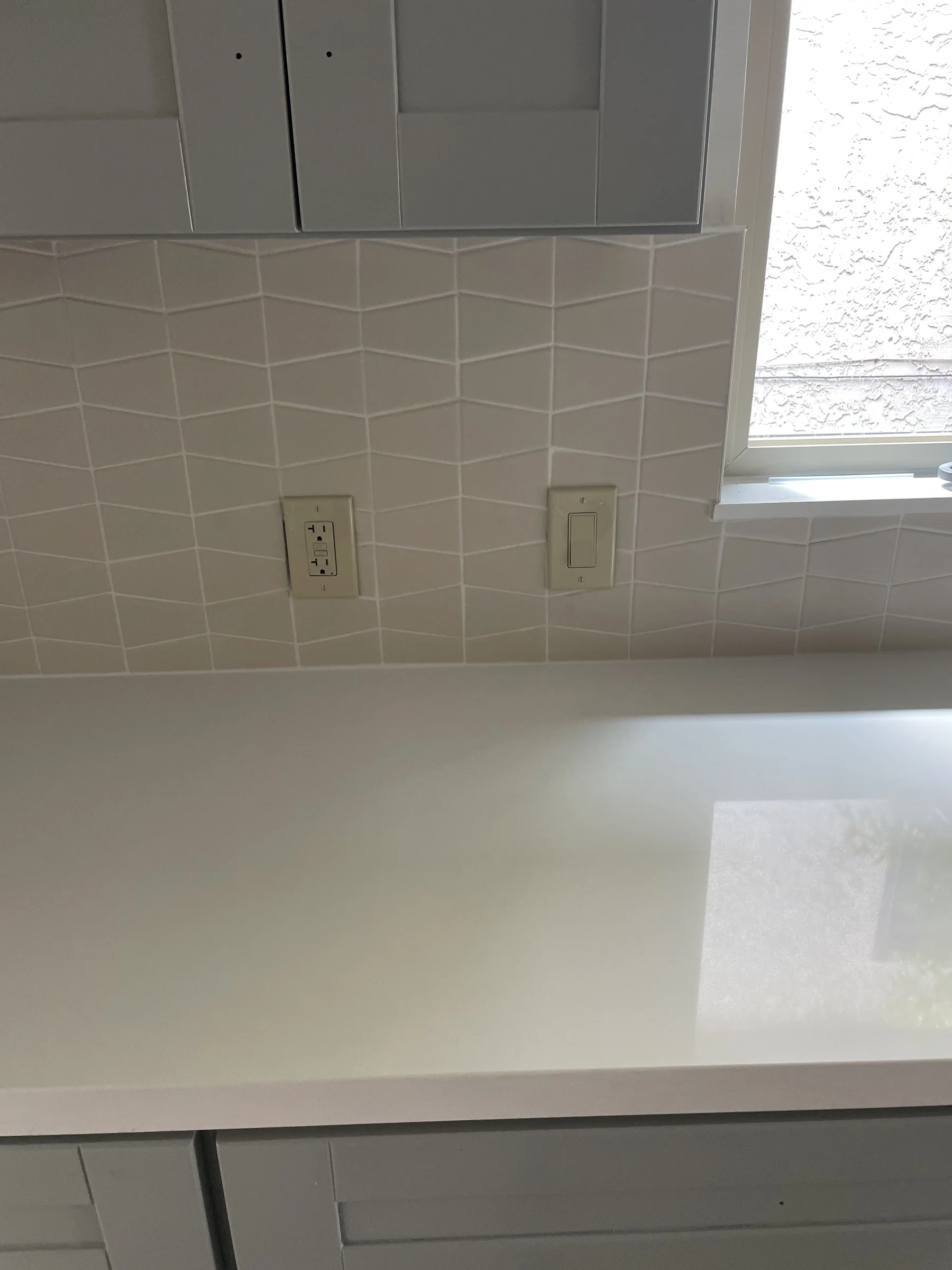 Close-up of a finished Alameda kitchen counter with white quartz and a white-on-white chevron tile backsplash under a window