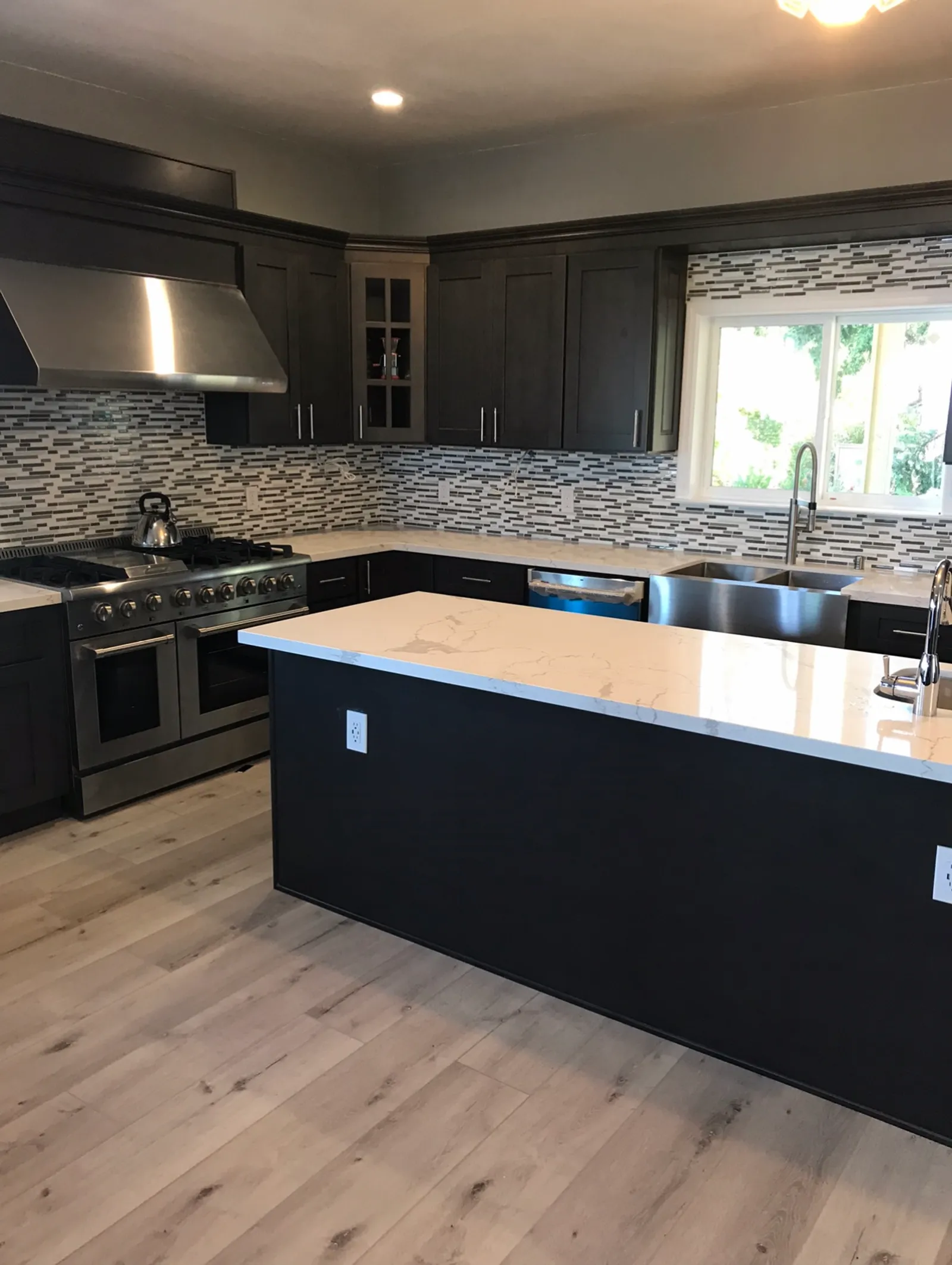 Dark cabinet kitchen with mosaic tile backsplash, quartz island, and professional range