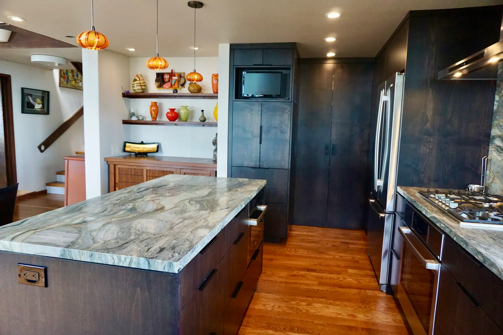 Modern kitchen with marble island, floating shelves, and dark cabinetry
