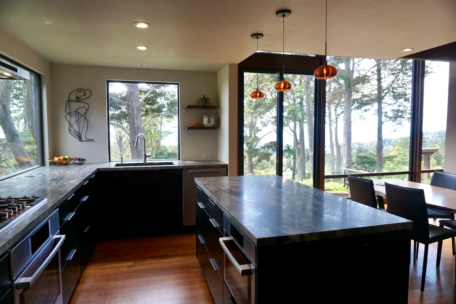 Open kitchen with marble countertops, floor-to-ceiling windows, and tree views
