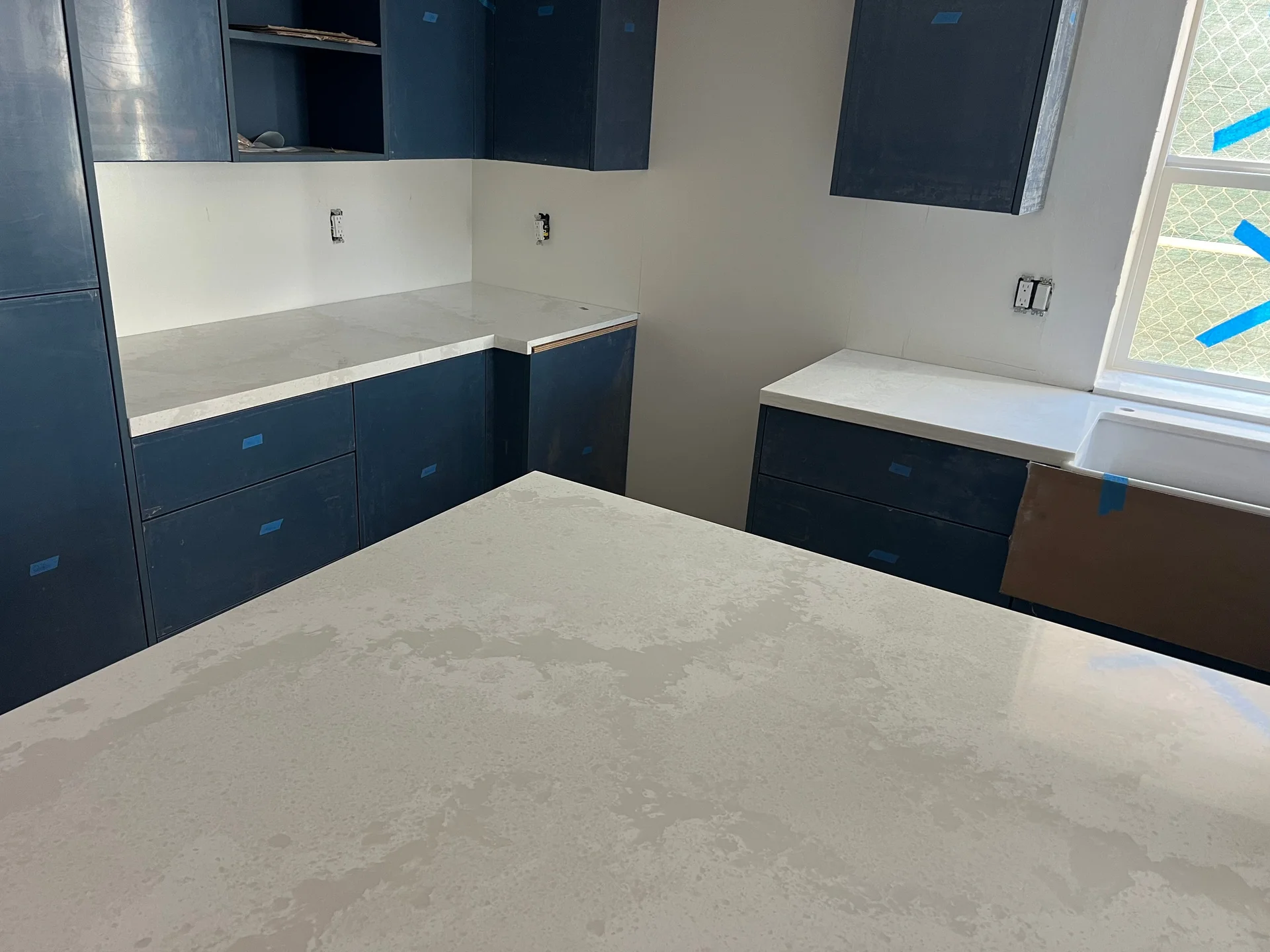 Navy cabinet kitchen with heavily-veined white quartz countertop and waterfall island edge