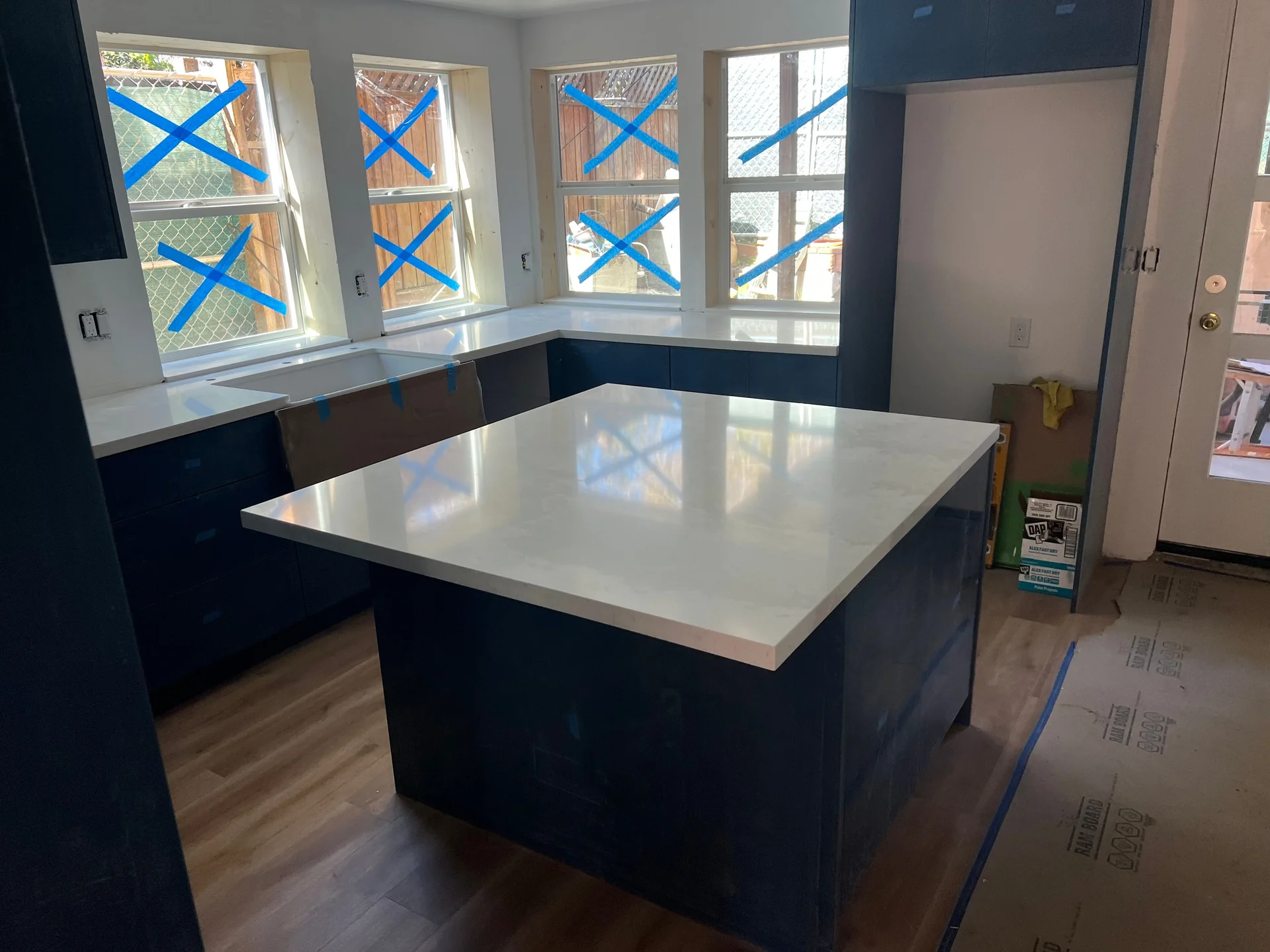 Wide-angle U-shape kitchen remodel with navy shaker cabinets, white quartz island, and light oak hardwood flooring
