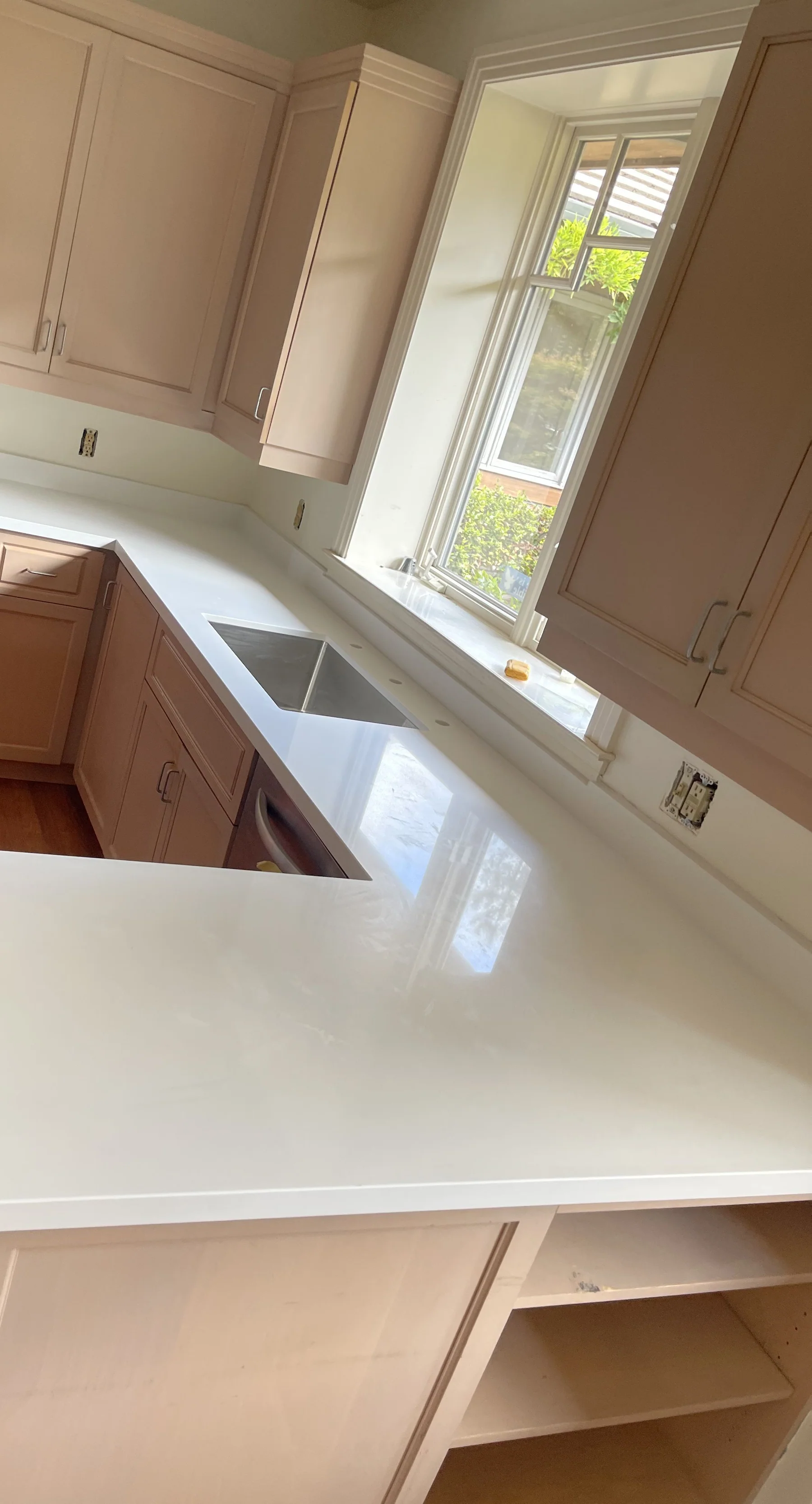 Mid-install white quartz countertop with angled peninsula in a Berkeley kitchen — cream shaker cabinets, casement window, hardwood floor