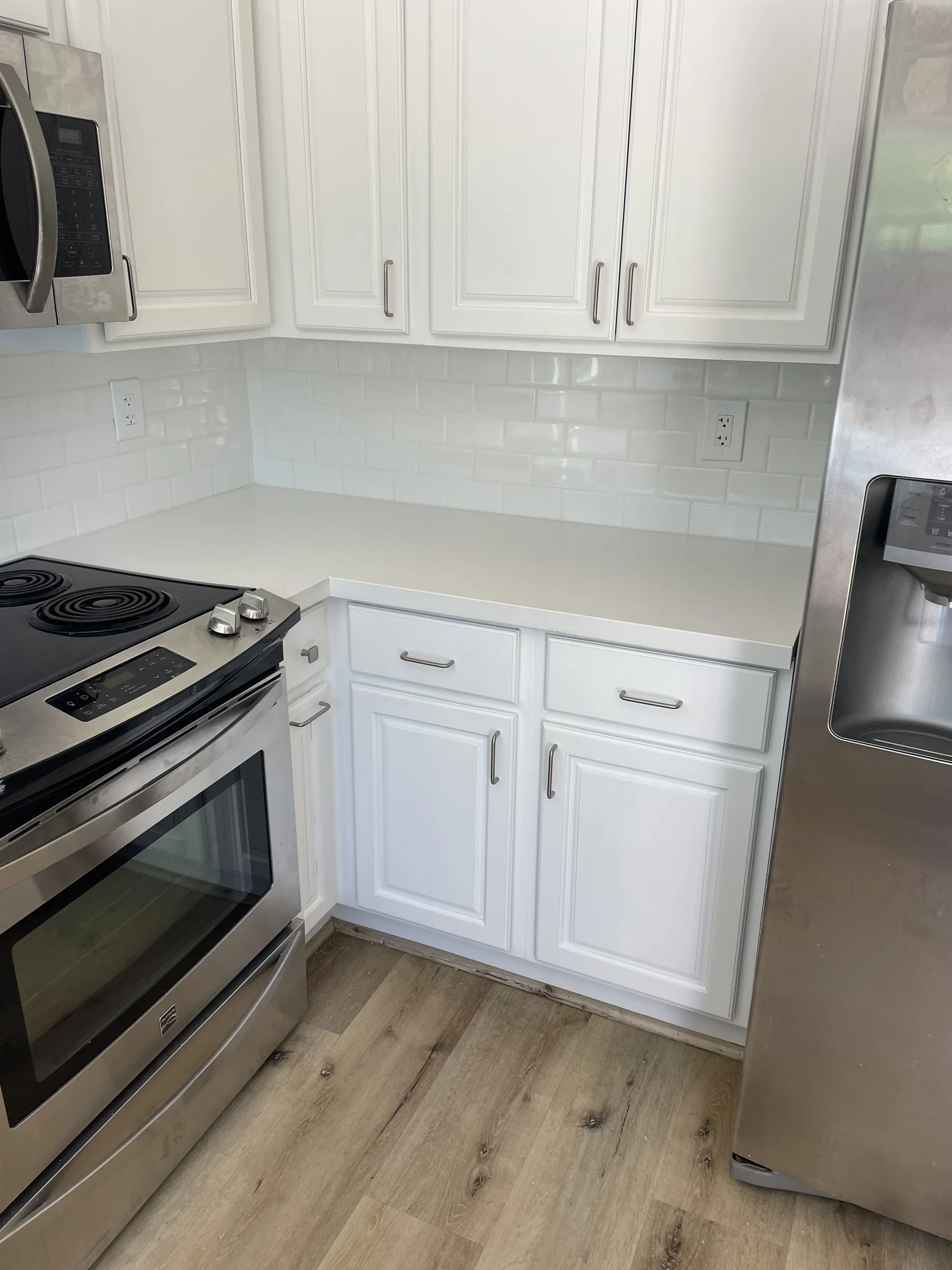 Finished Alameda kitchen with white raised-panel cabinets, white quartz countertop, white subway tile backsplash, stainless range and side-by-side fridge, and light Impala GAIA LVT flooring
