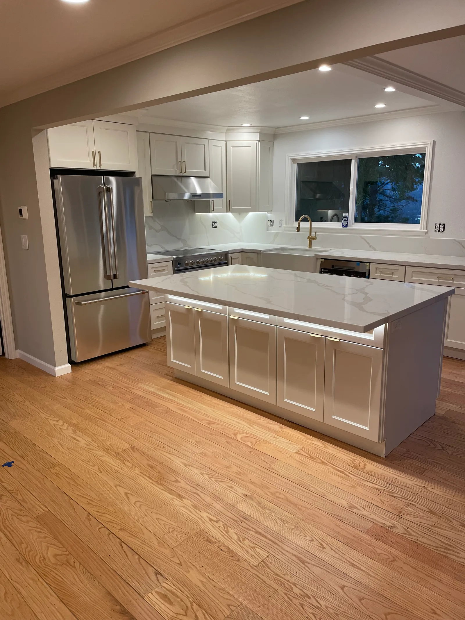 Kitchen island with quartz countertop, stainless fridge, and oak hardwood floors