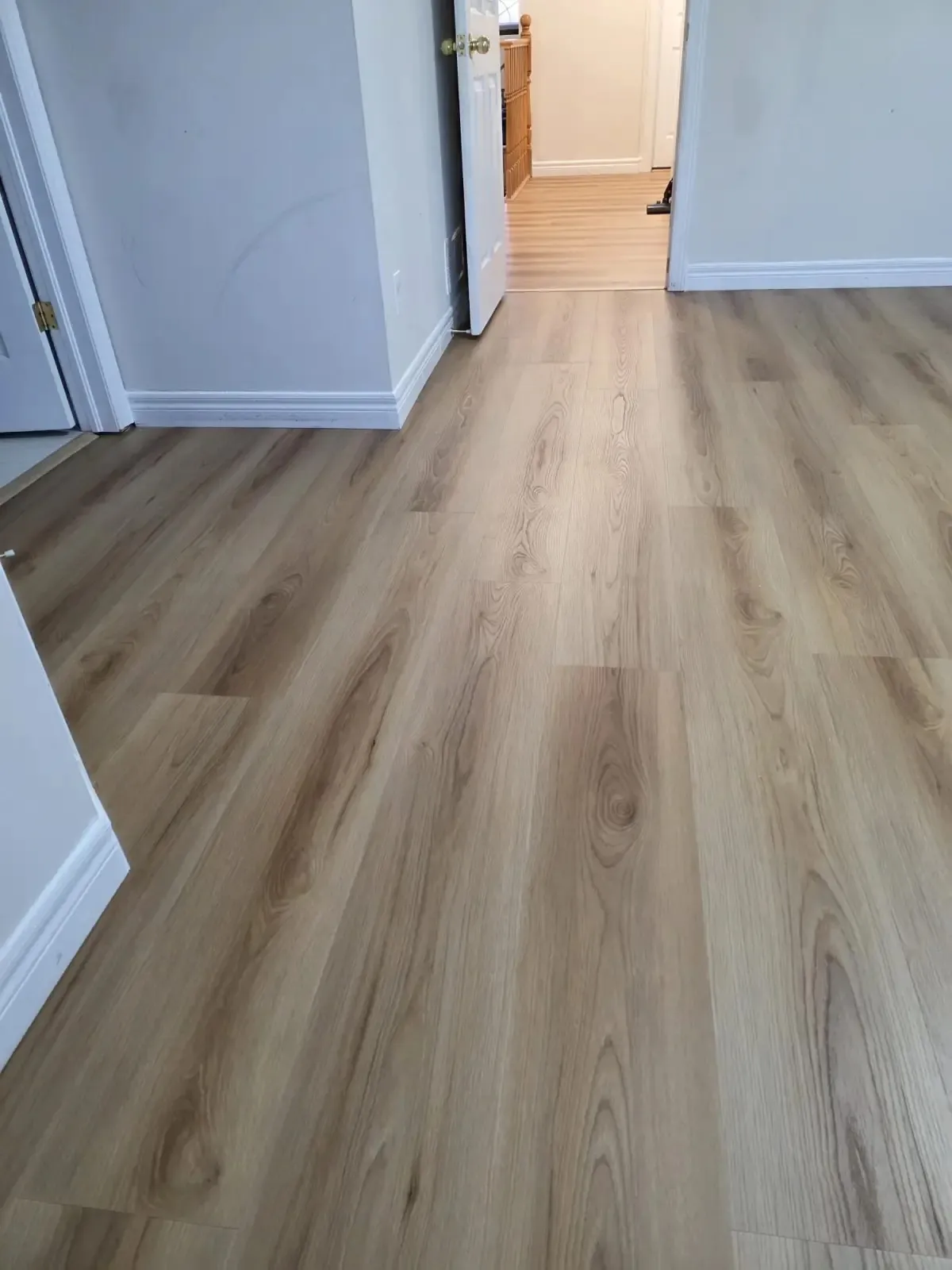 Luxury vinyl plank flooring in a hallway with warm oak tones and white baseboards